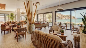 Un vaste espace de détente avec des meubles en osier, de grandes fenêtres donnant sur la plage et un arrangement décoratif en bambou.