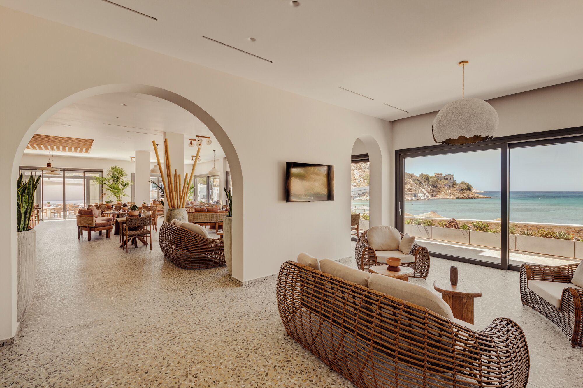 A spacious interior with a large window overlooking the sea, wicker furniture, and a view of a coastal landscape.