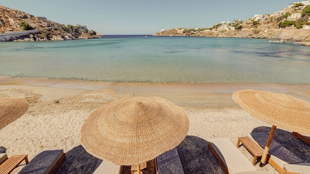 Une plage avec une eau cristalline, des chaises longues et des parasols en paille.
