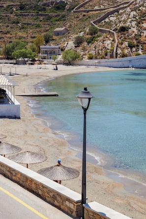 A beach with clear water, umbrellas, and a stone wall. - Armia Experience Hotel (Syros)