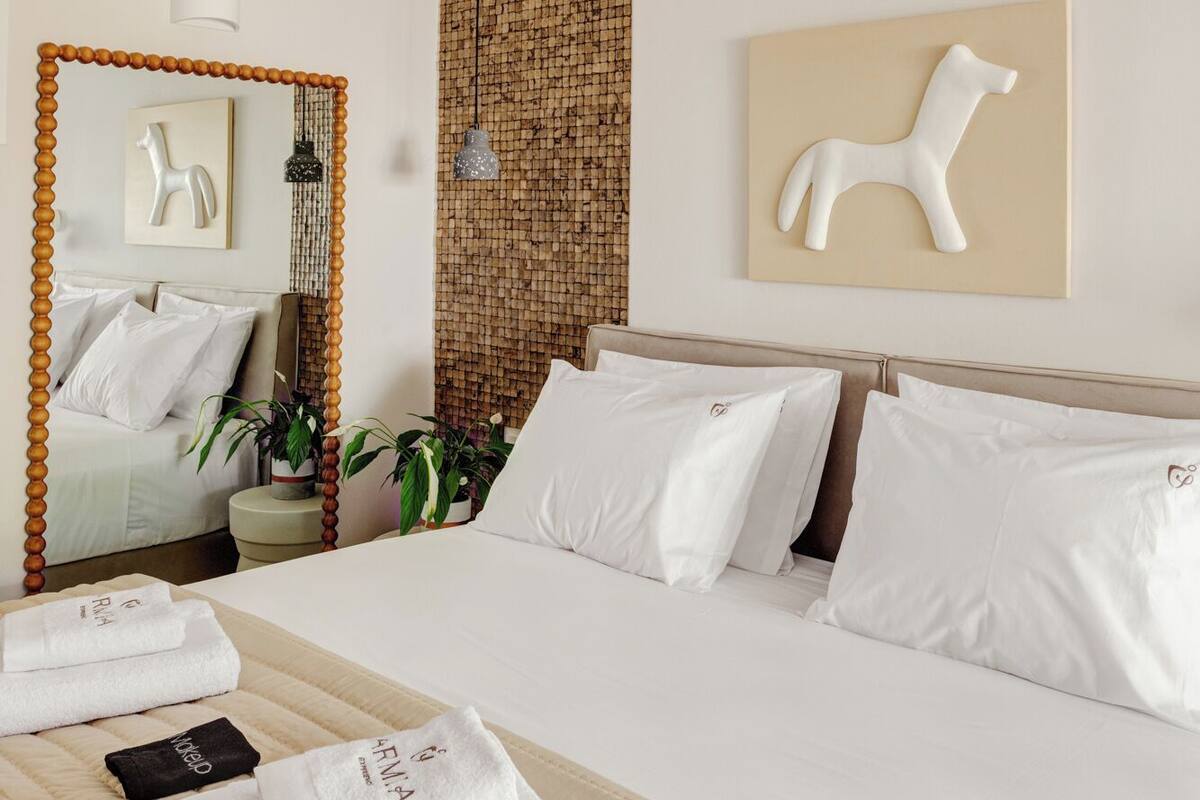 A hotel room with a large bed, a mirror, a wall-mounted artwork, and a textured wall panel.
