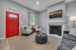 Ein Wohnzimmer mit roter Tür, Kamin, einem Gemälde und einem grauen Sofa.