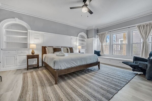Ein Schlafzimmer mit Bett, Nachttischen, einem Fenster mit Vorhängen und integrierten Regalen.