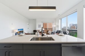 Eine moderne Küche mit einer großen Kochinsel, ein Essbereich mit einer Couch und Blick auf die Stadt durch große Fenster.