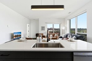Eine moderne Küche mit einer großen Kochinsel, ein Essbereich mit einer Couch und Blick ins Freie.