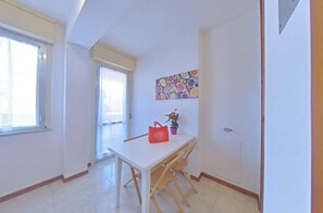 A room with a white table, a red bag, a potted plant, and a colorful wall art piece. - Seaside Escape for Four Guests (Lignano Sabbiadoro)
