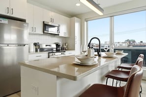 A modern kitchen with stainless steel appliances, a large island with seating, and a city view through the window. - Charming & Airy Two Bedroom Two Bathroom (Cleveland)