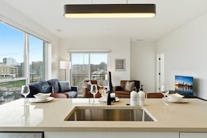 A modern kitchen with a large window, a dining area with a sofa, and a city view. - Charming & Airy Two Bedroom Two Bathroom (Cleveland)