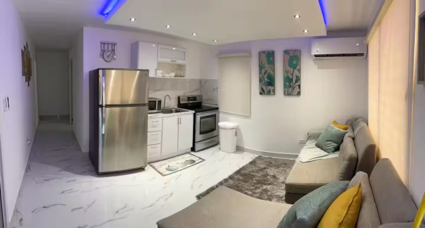 A modern kitchen with a refrigerator, microwave, and stove. There is a sofa and a rug in the living area.