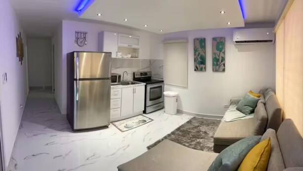 A modern kitchen with a refrigerator, microwave, and stove. There is a sofa and a rug in the living area. - Beautiful house minutes from airport and beach (Carolina)