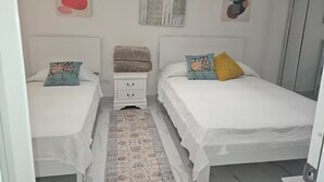A bedroom with two beds, a small white nightstand, a patterned rug, and abstract wall art. - Beautiful house minutes from airport and beach (Carolina)