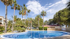 Piscina rodeada de palmeras y un muro de piedra.