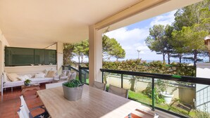 Un balcón amplio con vistas al mar, una mesa de madera con sillas, y una zona de estar con sofá y cojines.