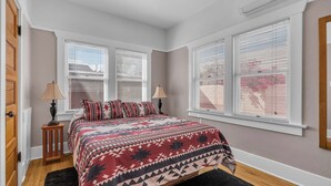 A bedroom with a bed, two windows with blinds, a nightstand, and a lamp. - Central Tucson Summer Retreat | Near UofA (Tucson)