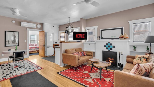 A modern living room with a fireplace, a sofa, a coffee table, and a television displaying 'NETFLIX'. - Central Tucson Summer Retreat | Near UofA (Tucson)