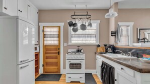A compact kitchen with a white refrigerator, stove, oven, and a microwave. There is a window with blinds, a sink, and a countertop with a dish rack. - Central Tucson Summer Retreat | Near UofA (Tucson)