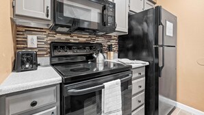 A kitchen with a microwave, stove, oven, refrigerator, and a tiled backsplash.