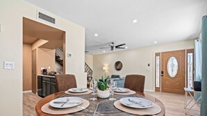 A dining area with a round table set for four, a ceiling fan, and a staircase leading to another level.
