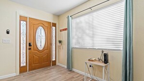 A hallway with a wooden door, a window with blinds, and a small table with a device on it.