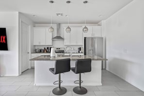A modern kitchen with white cabinets, a stainless steel refrigerator, and two bar stools. - Vail Summer Desert Retreat | Colossal Cave & Parks (Vail)