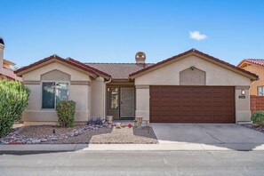 A single-story house with a brown garage door, a front door, and a small porch area. - Dove Mountain Home | Summer Family Retreat (Tucson)