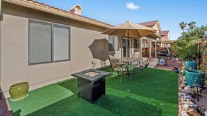 A patio with artificial grass, a fire pit, outdoor furniture, and a covered seating area.
