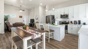 Una cocina moderna con armarios blancos, una isla central y un comedor con mesa y sillas de madera.
