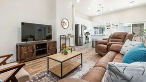 Una sala moderna con televisor, sofá, mesa de centro y una cocina al fondo.