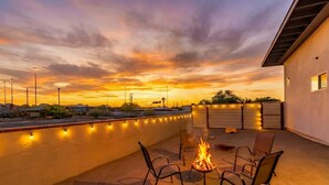 Un patio con una chimenea, sillas, una piscina y vistas al atardecer.