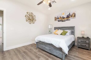 Ein Schlafzimmer mit einem Bett, einem Nachttisch, einem Wandbild und einem Deckenventilator.