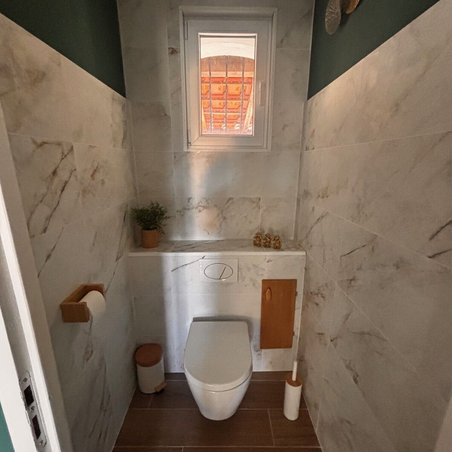 Ein kleines Badezimmer mit Toilette, Fenster, Waschbecken und Spiegel.