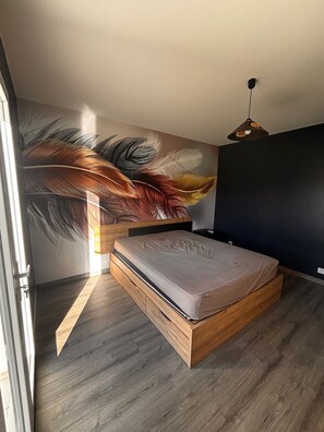 Ein Schlafzimmer mit Bett, Wandgemälde, Deckenleuchte und Fenster.