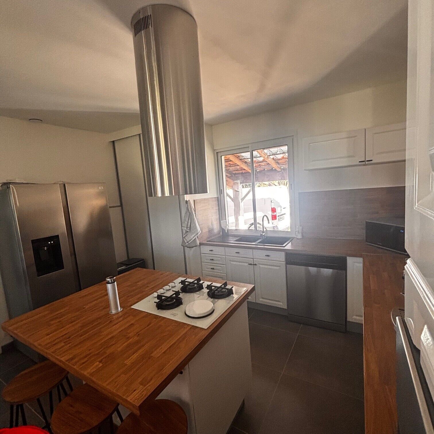 A modern kitchen with a central island, stainless steel appliances, and a view to the outside.
