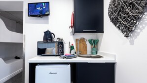 Una kitchenette compacta equipada con refrigerador, microondas, hervidor y un lavamanos pequeño.