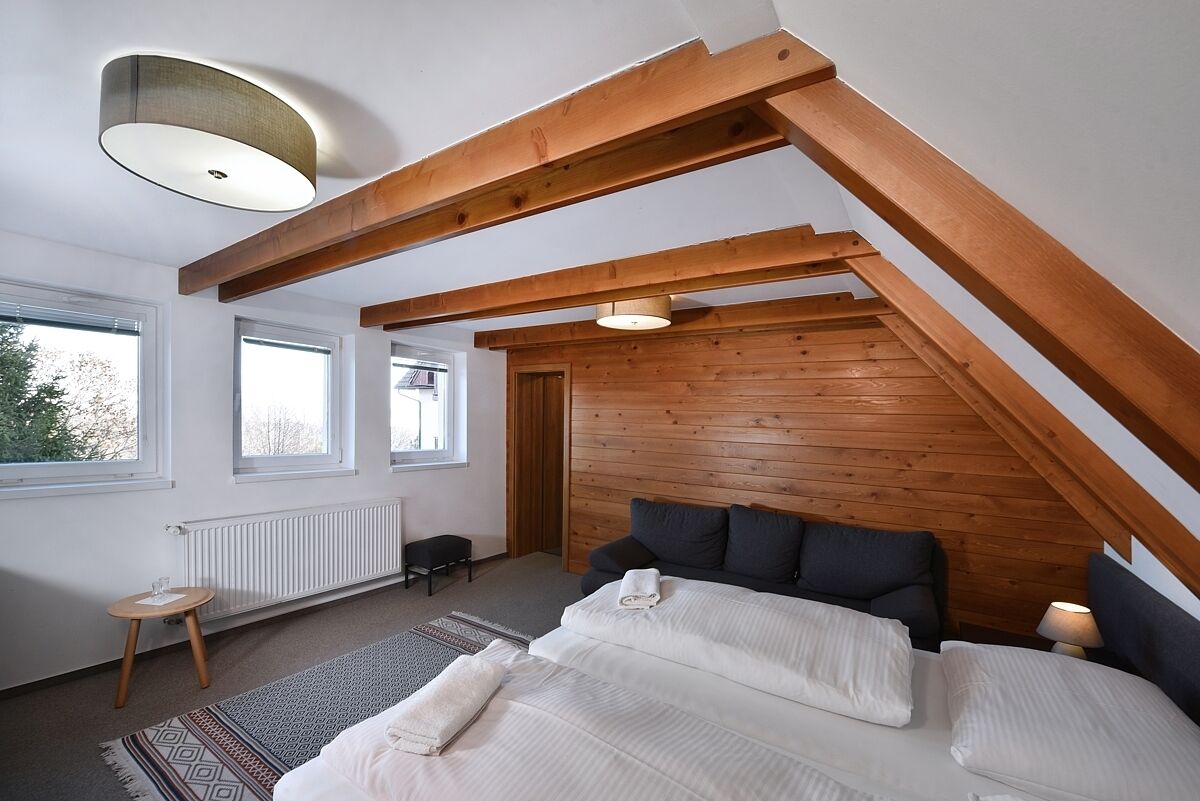 A bedroom with a sloped ceiling, wooden beams, a bed with pillows, a bedside table, and a window.