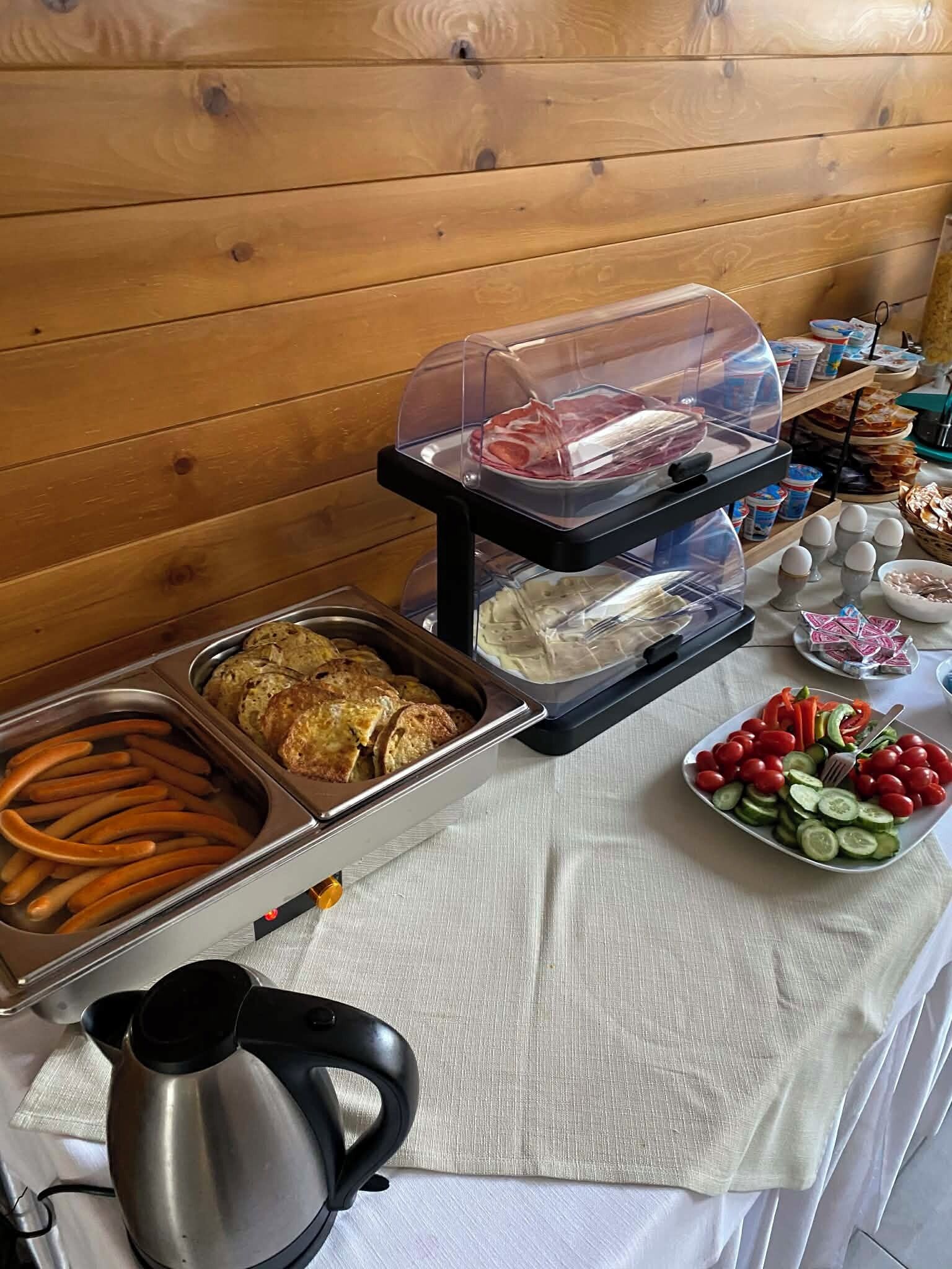 Un buffet proposant une variété de plats, notamment des viandes, des légumes et du pain, disposés sur une table avec une bouilloire.