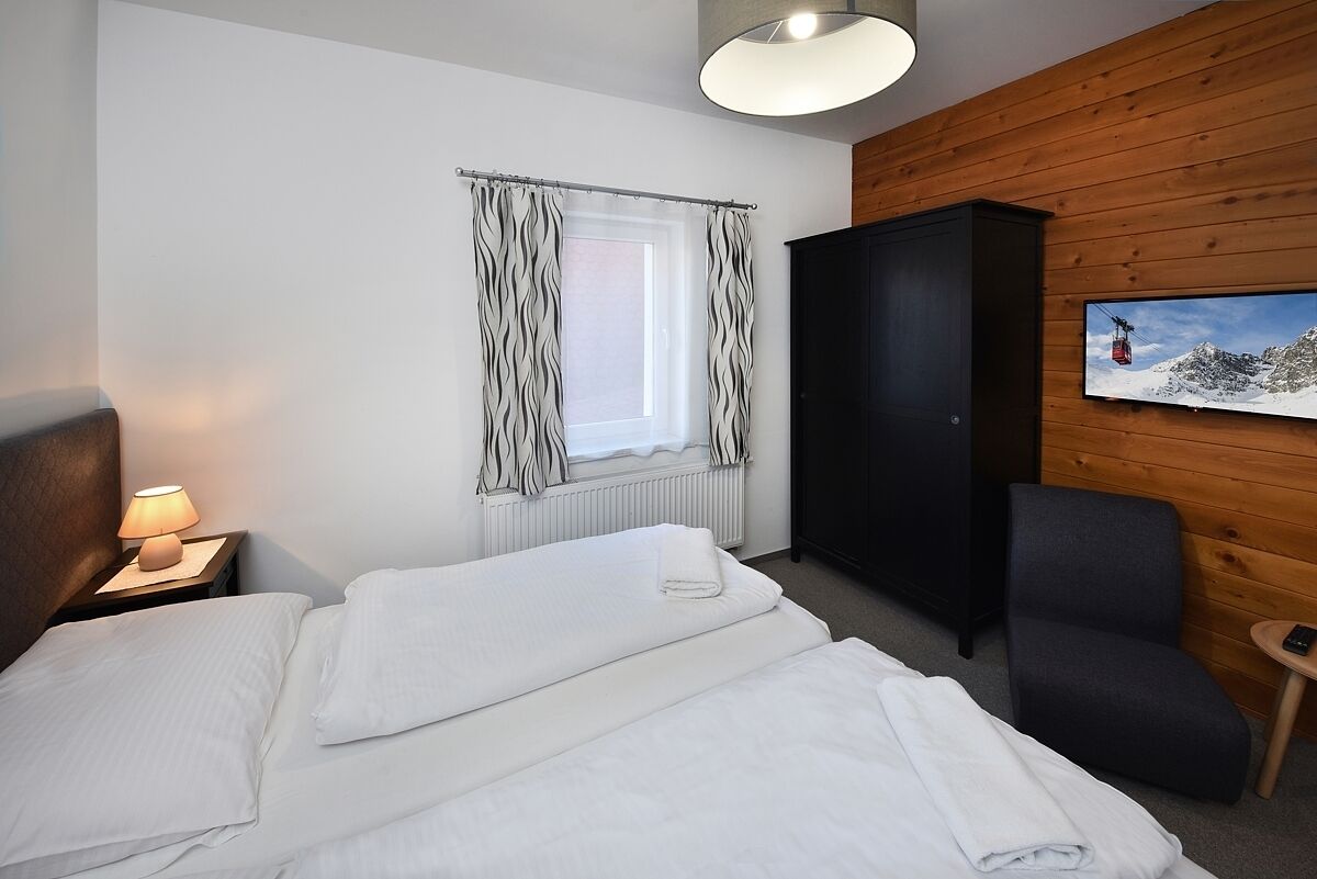 Une chambre d’hôtel comprenant un lit, une table de chevet avec une lampe, une fenêtre avec des rideaux, une armoire, une chaise et un tableau accroché au mur.
