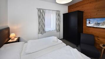Une chambre d’hôtel comprenant un lit, une table de chevet avec une lampe, une fenêtre avec des rideaux, une armoire, une chaise et un tableau accroché au mur.