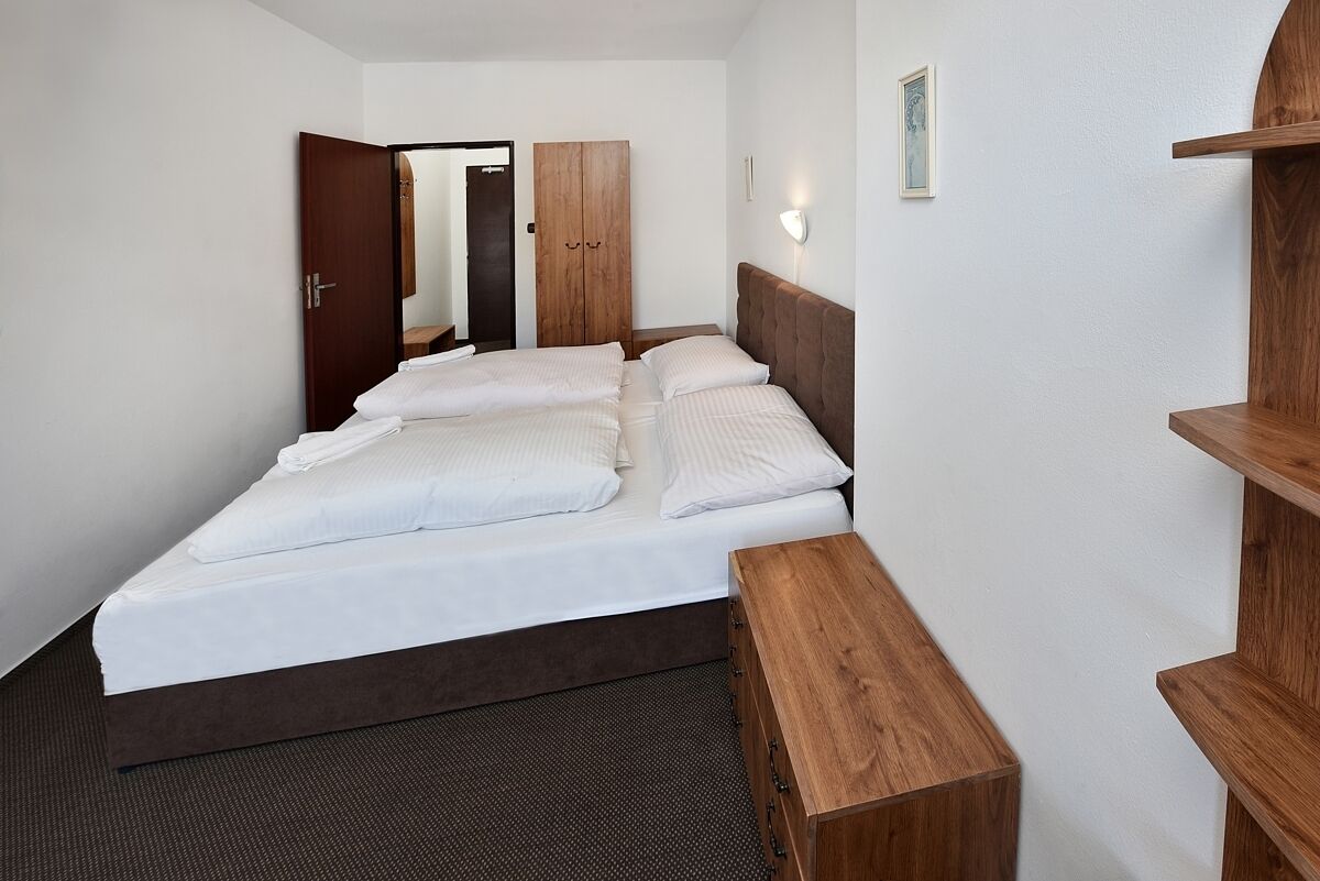 Ein Hotelzimmer mit einem Doppelbett, einem Holzschrank, einem kleinen Holztisch und einem an der Wand befestigten Regal.