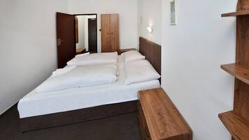 Ein Hotelzimmer mit einem Doppelbett, einem Holzschrank, einem kleinen Holztisch und einem an der Wand befestigten Regal.