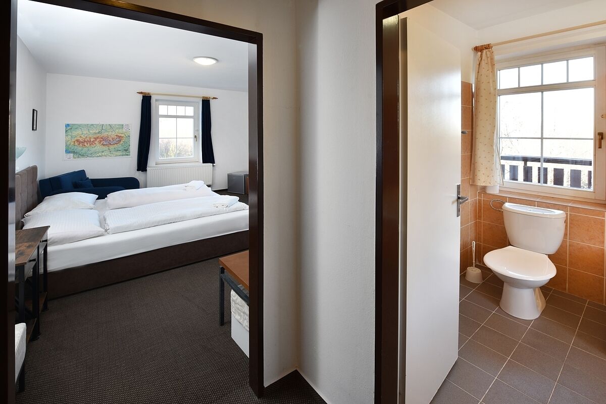 A hotel room with a bed, a desk, a window with curtains, a bathroom with a toilet and a window, and a map on the wall.