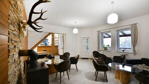 A room with a stone wall, a fireplace, a dining table with chairs, and a large window. - Penzión Chata Valaška (Vysoke Tatry)