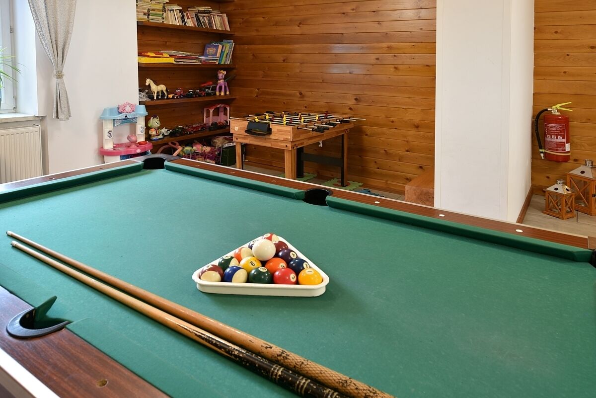 Une table de billard avec des queues et des billes, une table de baby-foot et une bibliothèque contenant divers objets.