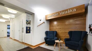 Un área de recepción con pared de madera, dos sillones azules, una pequeña mesa de madera y un letrero que dice 'pensión Valaška'.