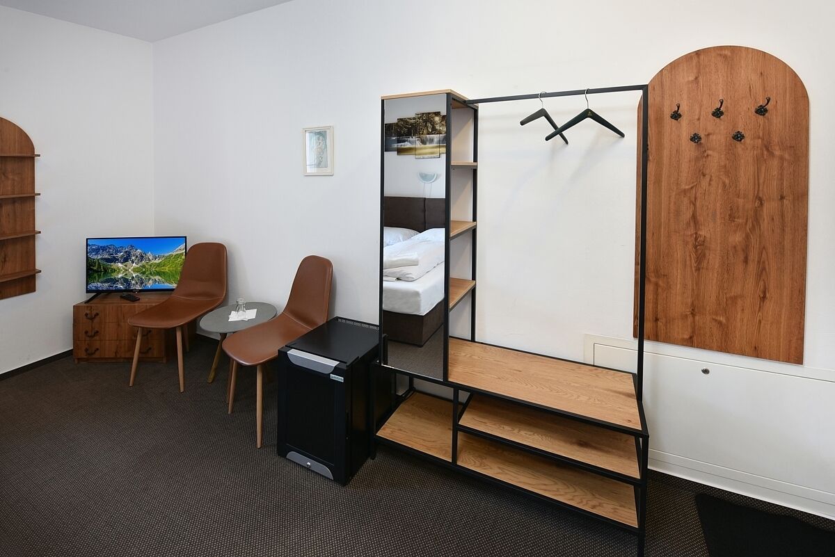 Une chambre d’hôtel de taille modeste, comprenant un lit, une télévision, un bureau, deux chaises, une armoire et un miroir.