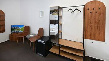 Une chambre d’hôtel de taille modeste, comprenant un lit, une télévision, un bureau, deux chaises, une armoire et un miroir.