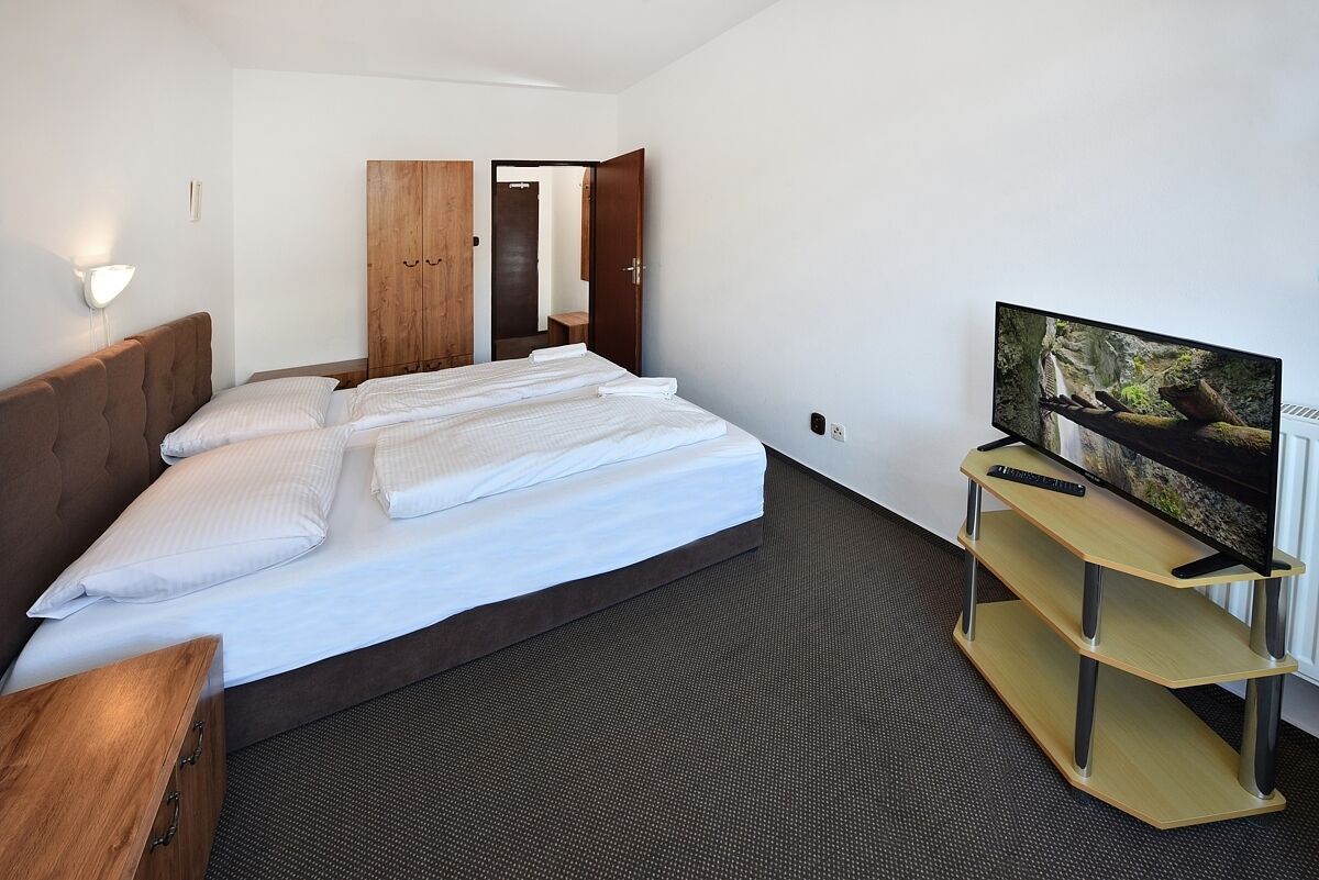 A hotel room with a bed, a TV on a stand, a wooden wardrobe, and a door leading to another room.