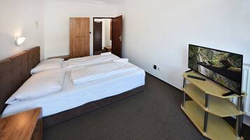A hotel room with a bed, a TV on a stand, a wooden wardrobe, and a door leading to another room.