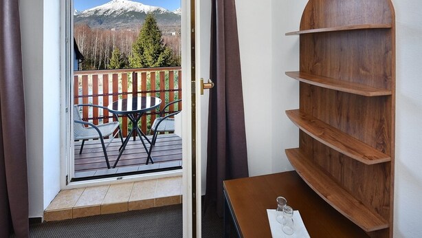 A room with a wooden shelf, a table with a glass, and a view of a deck with chairs and a mountain. - Penzión Chata Valaška (Vysoke Tatry)