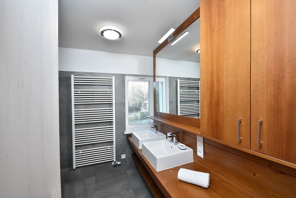 A modern bathroom with a large mirror, wooden vanity, two sinks, and a towel on the counter.